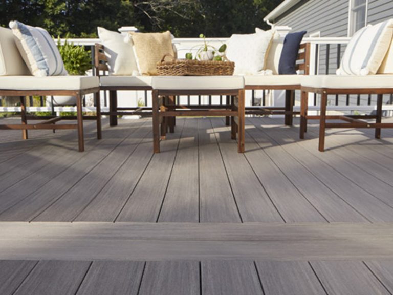 Outdoor seating area with cushioned wooden chairs on TimberTech Advanced PVC decking in a gray antique palm finish, surrounded by railing.