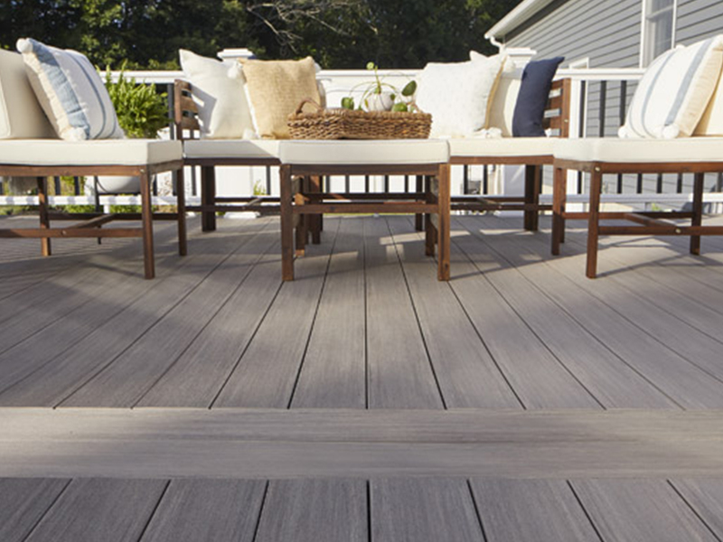 Outdoor seating area with cushioned wooden chairs on TimberTech Advanced PVC decking in a gray antique palm finish, surrounded by railing.